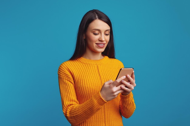 Sonriente joven sostiene celular moderno envía mensaje en redes sociales