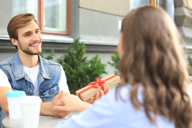 Foto sonriente joven tener una cita con su novio en la cafetería, hombre con caja actual.