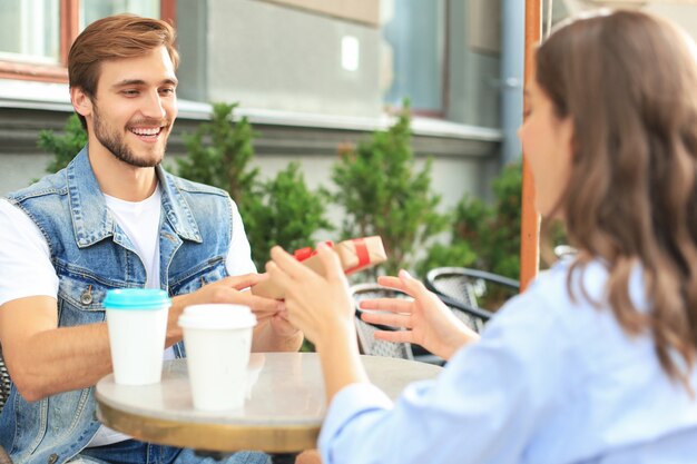 Sonriente joven tener una cita con su novio en la cafetería, hombre con caja actual.