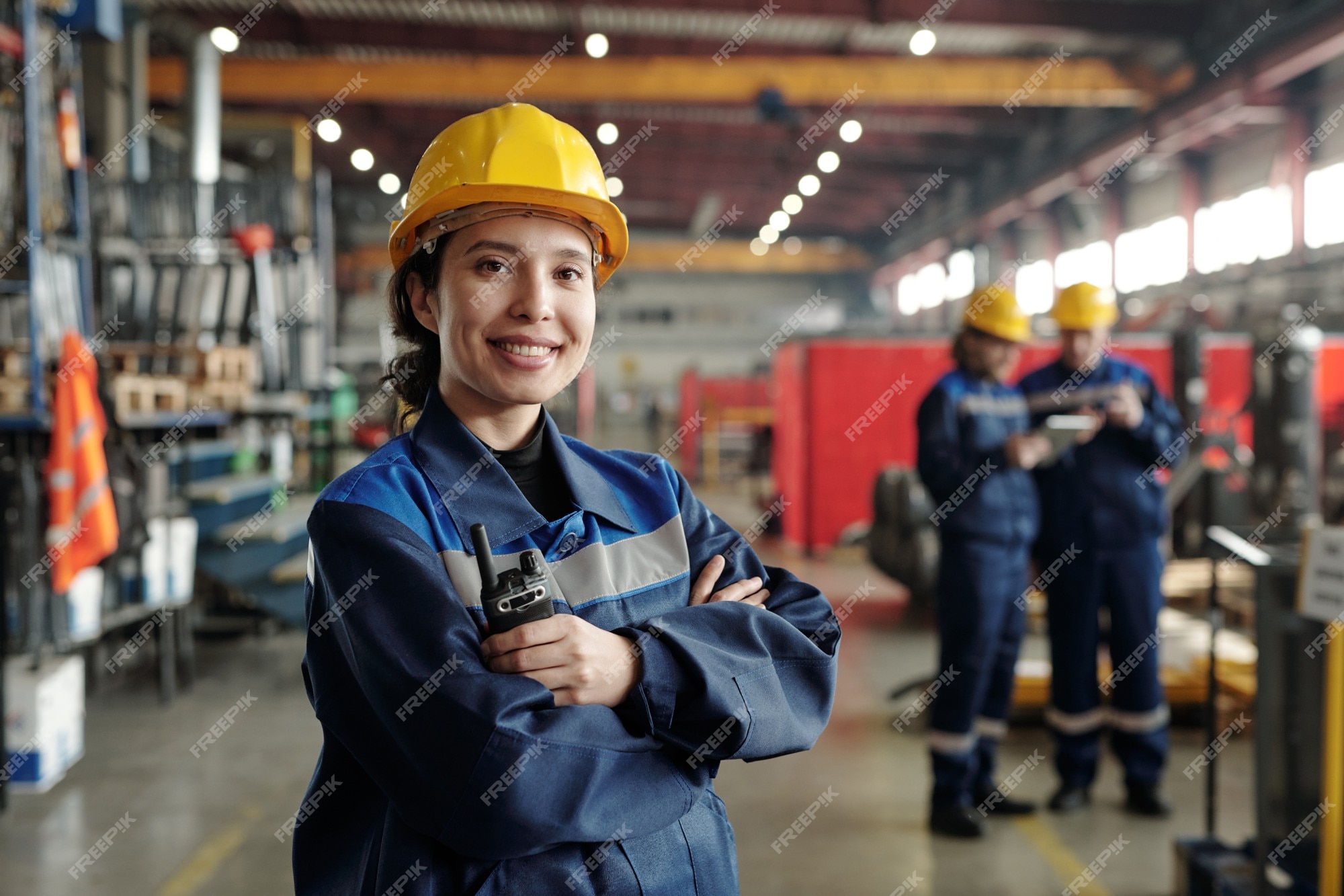 Sonriente joven trabajadora de la moderna planta industrial o fábrica en ropa de trabajo y casco protector de pie en un gran taller Foto Premium