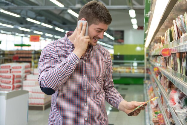 Sonriente joven a través de teléfono móvil mientras compras en la tienda de compras