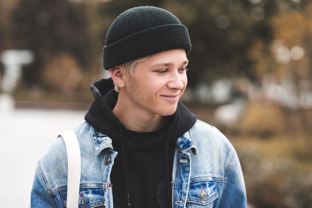 Sonriente jovencito vistiendo gorro de punto negro con capucha y chaqueta vaquera