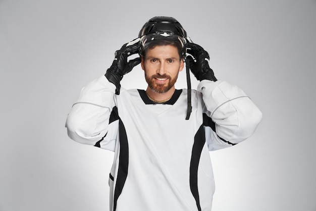 Foto sonriente jugador de hockey sobre hielo barbudo poniéndose un casco protector en el interior retrato de un deportista masculino