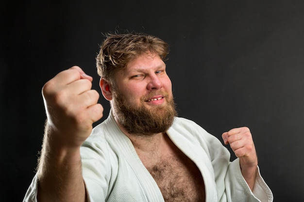 Sonriente karateca barbudo en kimono blanco muestra puños