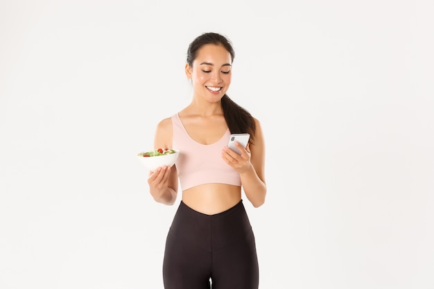 Sonriente linda chica asiática con aplicación de dieta, aplicación de seguimiento de calorías en el teléfono móvil, tiene ensalada.