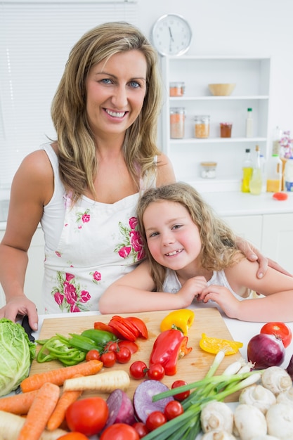 Sonriente madre e hija de pie en la mesa llena de verduras