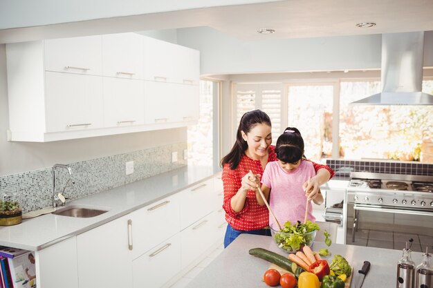 Sonriente madre e hija preparando ensalada de verduras