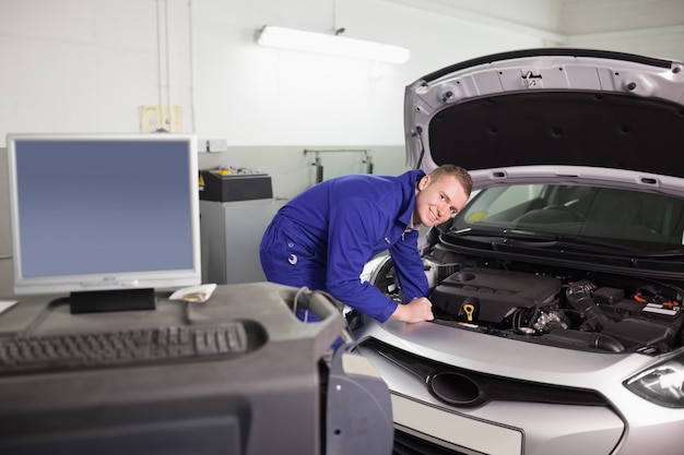 Sonriente mecánico examinando un motor de un automóvil