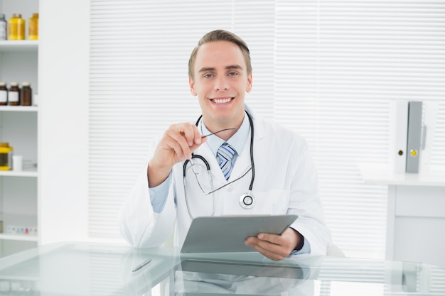 Sonriente médico masculino con tableta digital en consultorio médico