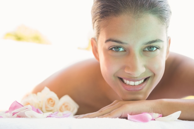 Foto sonriente morena acostada en una toalla con pétalos de rosa