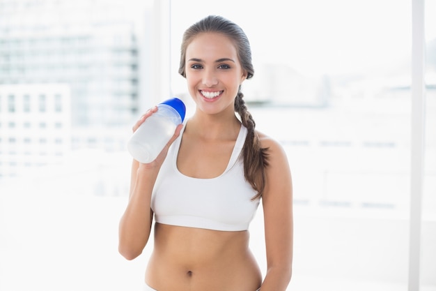 Sonriente morena deportivo sosteniendo una botella de agua