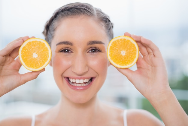 Sonriente morena saludable con rodajas de naranja