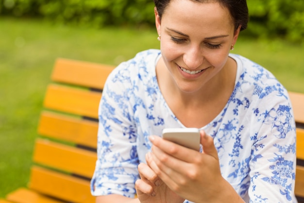 Foto sonriente morena sentada en el banco de mensajes de texto