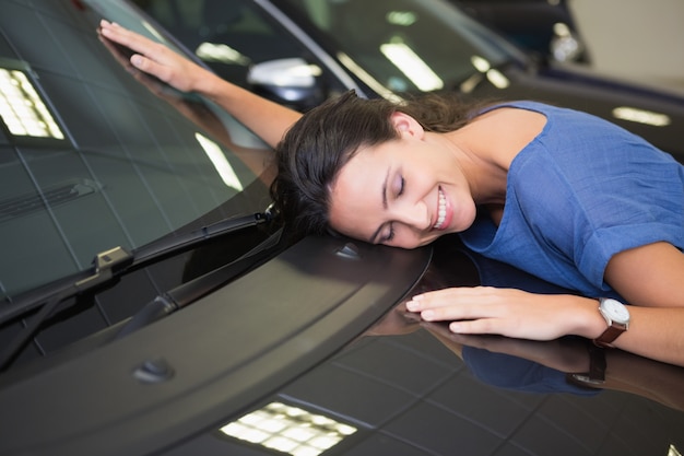 Sonriente mujer abrazando un auto negro