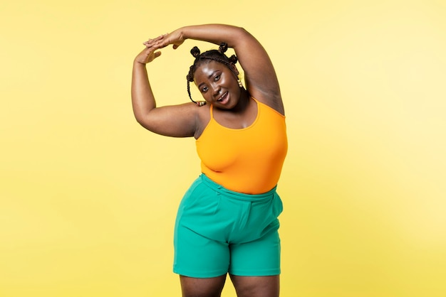 Sonriente mujer africana atractiva haciendo ejercicios mirando a la cámara aislada en fondo amarillo Concepto de tamaño Plus estilo de vida saludable