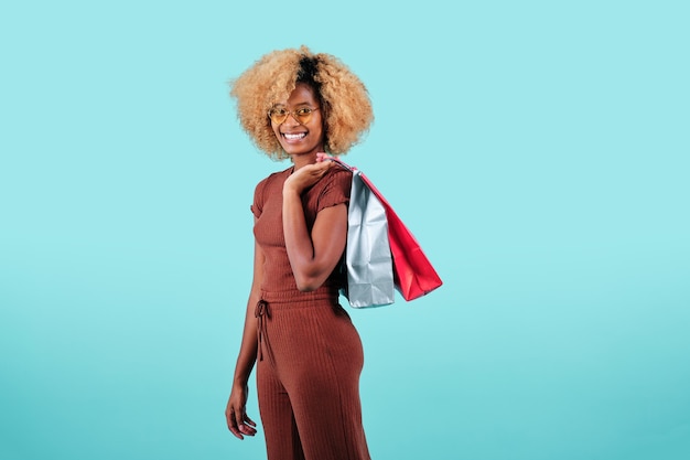 Sonriente mujer afro llevando bolsas de papel de compras de colores sobre un fondo aislado. Concepto de ventas de viernes negro.