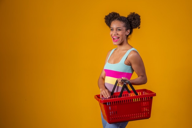 Sonriente mujer afro sosteniendo la cesta de la compra vacía mirando a la cámara sonriendo