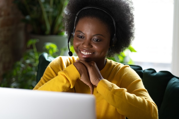 Sonriente mujer afro usar auriculares hablar videollamadas, usar una computadora portátil, ver el trabajo del seminario web desde casa