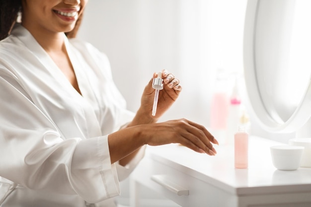 Sonriente mujer afroamericana aplicando suero en su mano en casa