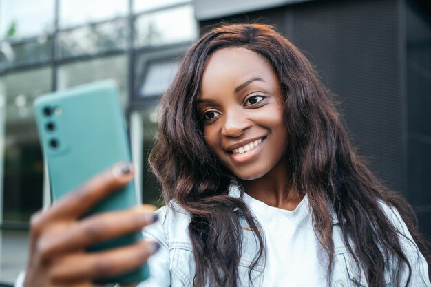 Sonriente mujer afroamericana de pie fuera tomando selfie