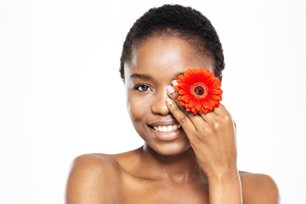 Sonriente mujer afroamericana posando con flor aislado sobre un fondo blanco.