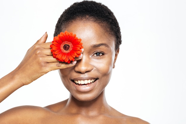 Sonriente mujer afroamericana que cubre el ojo con flor aislado sobre fondo blanco.