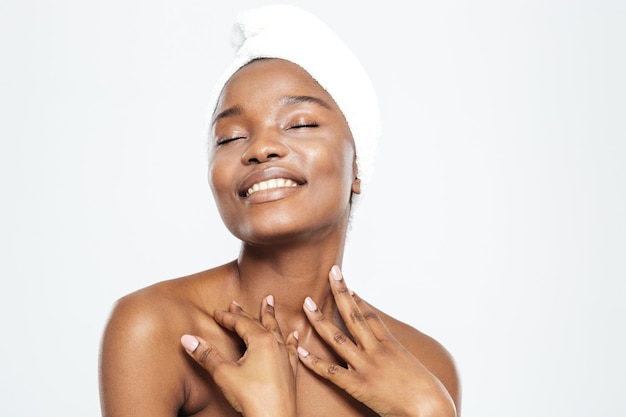 Sonriente mujer afroamericana relajada con una toalla en la cabeza que se encuentran aisladas sobre un fondo blanco.