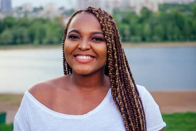 Sonriente mujer afroamericana sosteniendo la bandera de EE.UU. y mirando a la cámara primavera tarde de otoño en el parque junto al lago