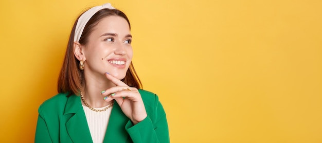 Sonriente mujer alegre con chaqueta verde parada aislada sobre fondo amarillo mirando hacia el espacio publicitario para el texto promocional