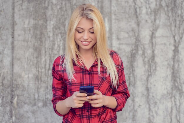 Sonriente mujer alegre feliz con cabello rubio, en camisa a cuadros con móvil 3g, 4g interent para chatear y enviar mensajes.