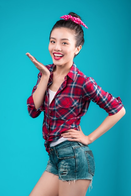 Sonriente mujer asiática encantadora vestida con un vestido estilo pin-up sobre azul.