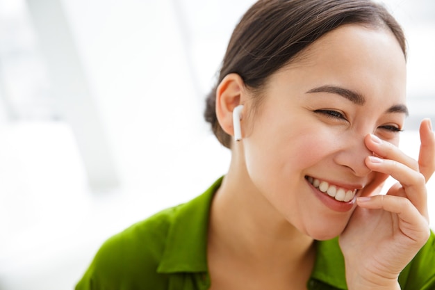 Sonriente mujer asiática escuchando música con auriculares en el interior