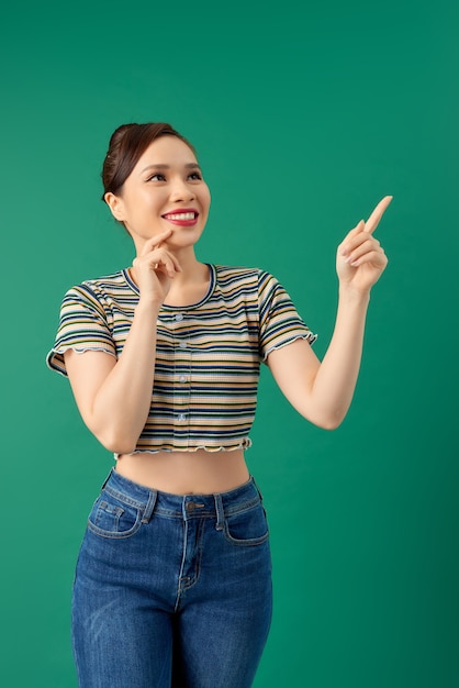 Sonriente mujer asiática joven feliz apuntando con su mano sobre verde.