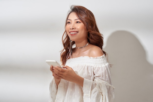 Sonriente, mujer asiática positiva con hermoso rostro emocional escuchando música sobre blanco