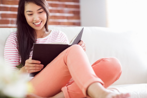 Sonriente mujer asiática en sofá leyendo