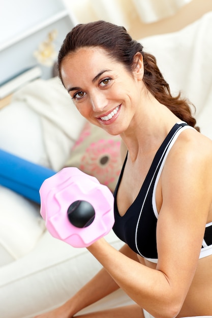 Sonriente mujer atlética sosteniendo una pesa en su sala de estar