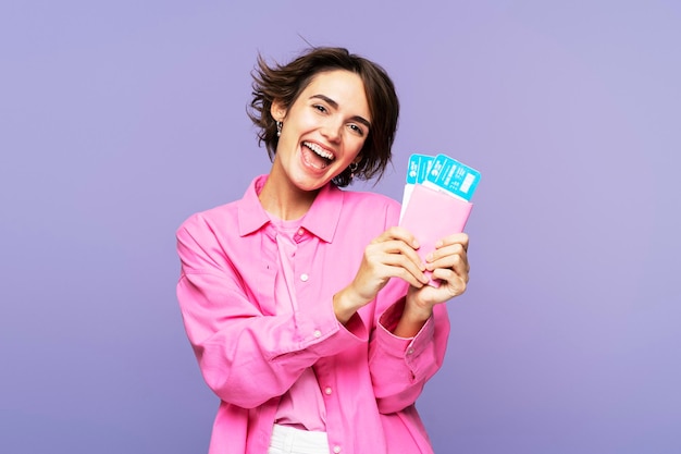 Sonriente mujer atractiva de color rosa con cabello moreno sosteniendo boletos de viaje y documentos