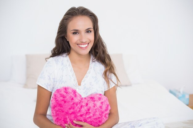 Sonriente mujer atractiva con corazón almohada