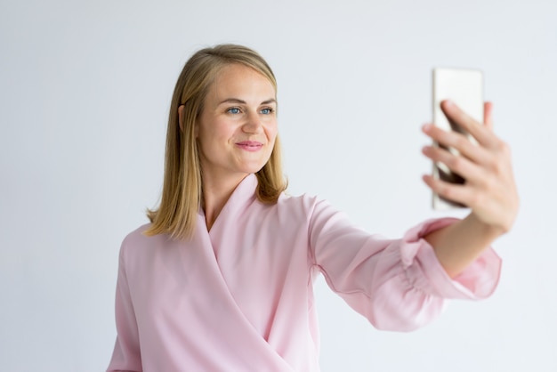 Sonriente mujer atractiva tomando selfie en teléfono.