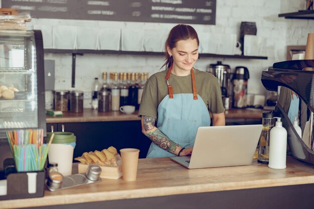 Sonriente mujer barista usando notebook en cafe