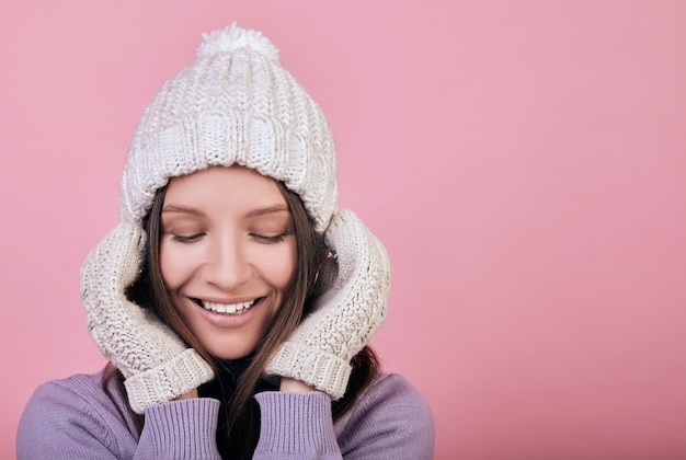 Sonriente mujer de belleza con los ojos cerrados en un sombrero de punto blanco invierno y guantes blancos