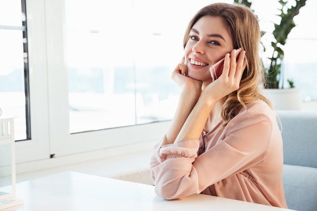 Sonriente mujer blondy en blusa sentada junto a la mesa