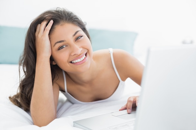 Sonriente mujer casual usando laptop en la cama