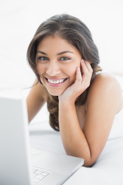 Sonriente mujer casual usando laptop en la cama