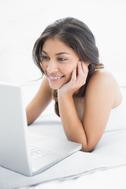 Sonriente mujer casual usando laptop en la cama