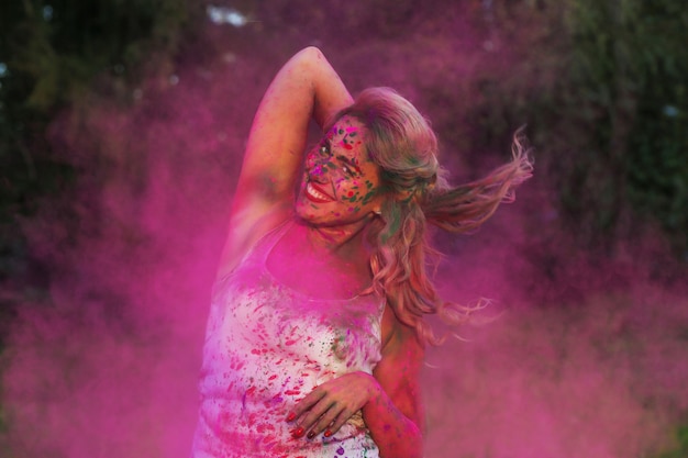 Sonriente mujer caucásica en una nube de pintura seca rosa, celebrando el festival de Holi