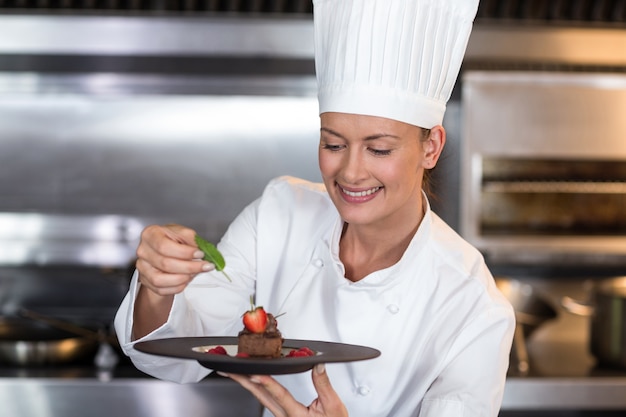 Sonriente mujer chef con plato de comida en la cocina