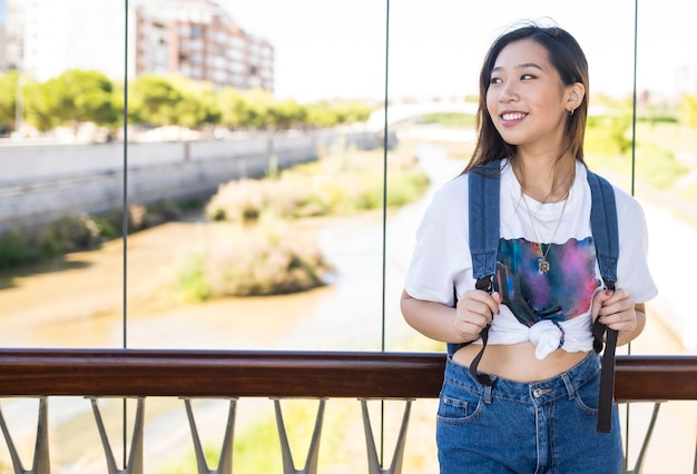 Sonriente mujer China con mochila en un puente un día soleado