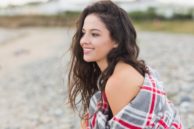 Foto sonriente mujer cubierta con una manta en la playa