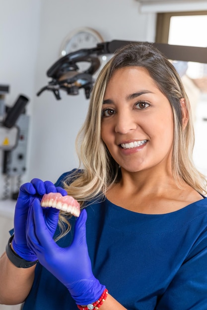 Sonriente mujer dentista sosteniendo modelo dental en la clínica